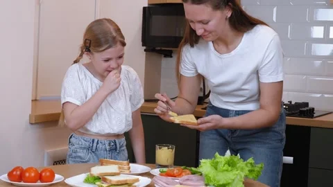 Mom spreading mustard on slice of bread for daughter making sandwich together Stock Footage 317819209