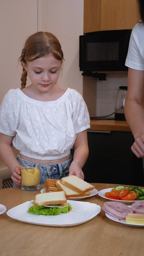 Mom spreading mustard on slice of bread for daughter making sandwich together Stock Footage 317819644