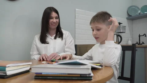 Mom talking to her son while he is drawing in a notebook sitting at the table Stock Footage 262032206