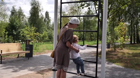 Mom talks a two-year-old toddler out of climbing adult stairs at the playground Stock Footage 273611514