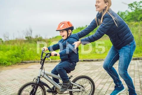 Mom teaches son to ride a bike in the park Stock Photos