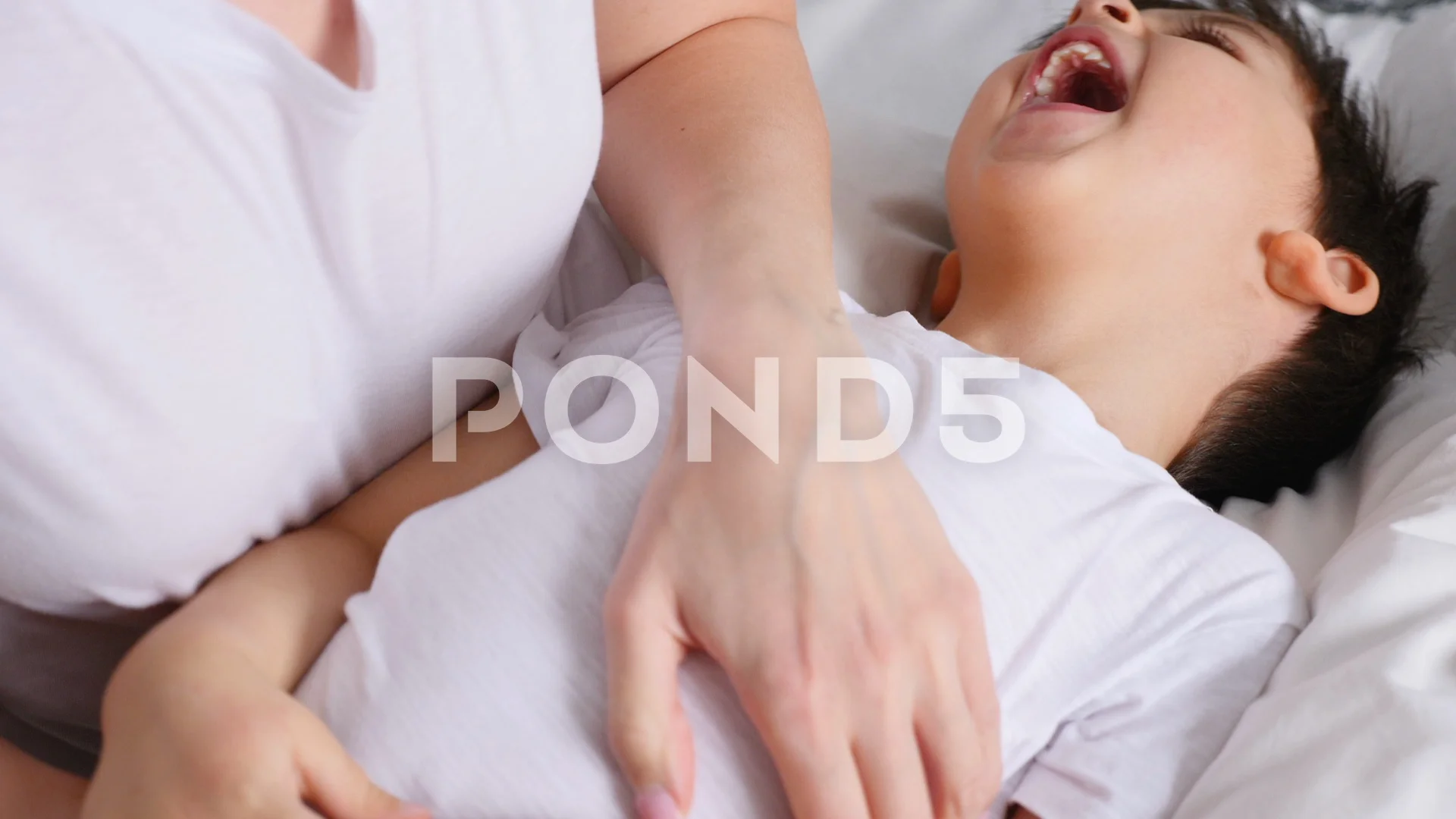 mom tickles her little son lying on the bed