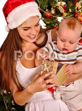 Mom wearing Santa hat holding kid under Christmas tree Stock Photos