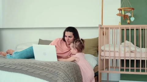 Mom works using laptop while lying on bed with baby Stock Footage 156473782