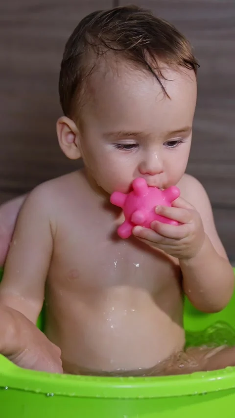Mom's hands washing her son sitting in a washbowl. Lovely kid is focused on the Stock Footage 342249153