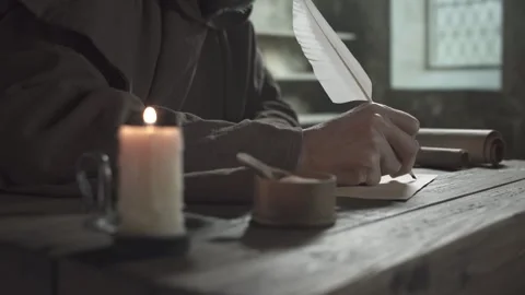 Monastic scribe in a brown robe writing with a long white feather pen on a page Stock Footage 338990494