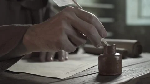 Monastic scribe dipping a feather quill pen into a clay inkpot on a table Stock Footage 337648936