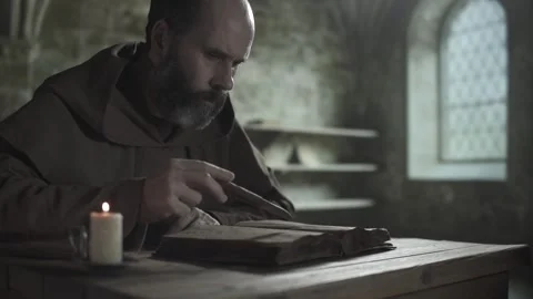 Monastic scribe reading book, following text lines with a penknife, dark library Stock Footage 339230963