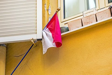 A Monegasque flag pressed against an open window shutter on the wall Stock Photos