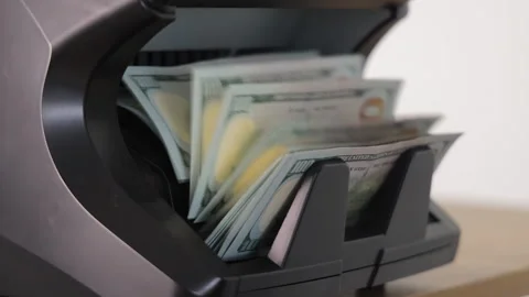 Money counter machine counting stack of US dollars, close-up on cash flow and Stock Footage 309401109