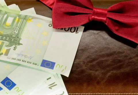 Money in an envelope on a brown notepad background and red bow tie Stock Photos