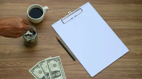 Money saving, hand puts US Dollar coin in glass jar with coffee, note paper Stock Footage 80906548