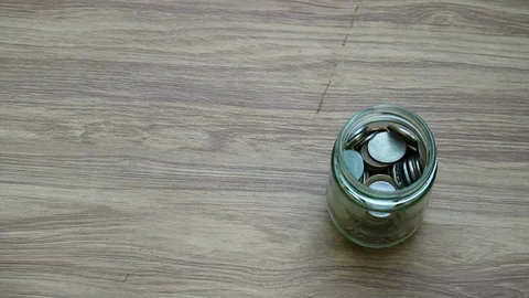 Money saving, hand puts US Dollar coin in glass jar on wood table Stockbeeldmateriaal 80906639