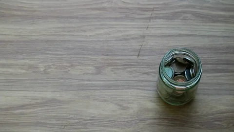 Money saving, hand puts US Dollar coin in glass jar on wood table Stockbeeldmateriaal 80907475