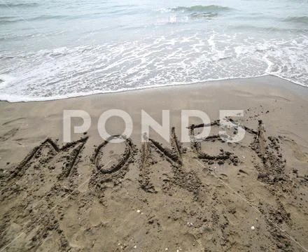 MONEY text written on the sand of the beach near the sea and the incoming wav Stock Photos