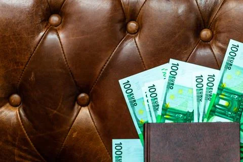 Money under a notepad on a leather sofa. The concept of wealth. Stock Photos