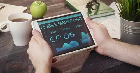 Monitoring mobile marketing data using tablet computer at desk Stock Footage