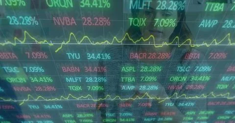 Monitoring two analysts reviewing data in office, with stock tickers, line graph Stock Photos