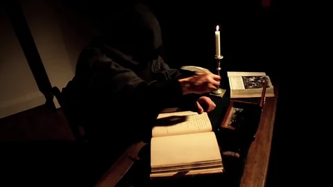 A monk, in a black cassock, with a hood, writes, with a goose quill, in a book,  Stockbeeldmateriaal 79686607