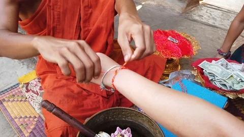  The monk blesses the tourists by tying a red ribbon on their hands Stock Footage 106826422