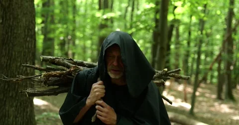 Monk carries a bundle of firewood on his shoulder moving through the forest amon Stock Footage 336694989