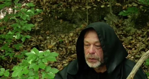 Monk in a dark cloak sits in the forest with closed eyes during prayer or medita Stock Footage 336693550