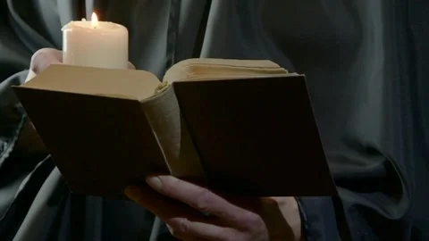 Monk holding candle and reading open book in dim dramatic light Stock Footage 342511162