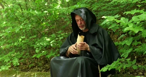 Monk sits in the forest and takes out a scroll for reading or study during a sol Stock Footage 336694123