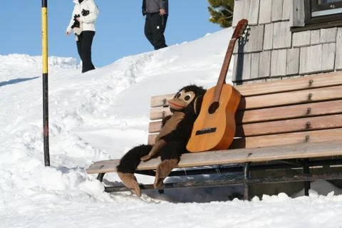 A monkey puppet sits close to a guitar on a bench in the snow Stockfoto's