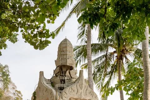 Monkey standing on ornate temple structure surrounded by palm trees 库存照片