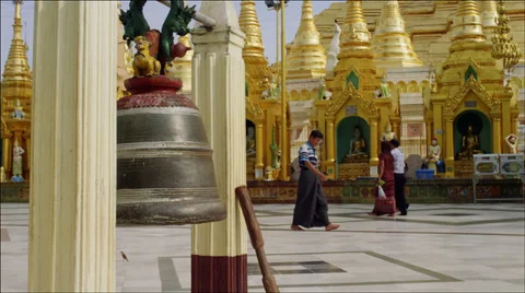 Monks and devotees walk past large bell at Shwedagon Pagoda Video stock 33625301