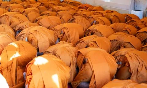 Monks bow forward together in a packed indoor ritual. Orange robes cover th.. Stock Photos
