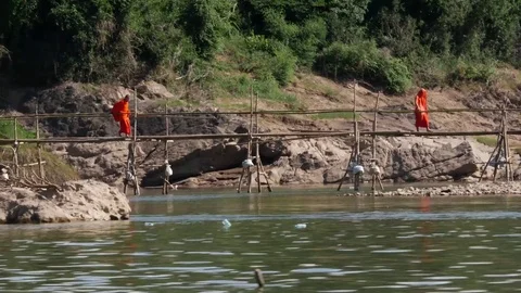 Monks crossing an old bamboo bridge across the River in Luang Prabang Laos Stock Footage 74684335