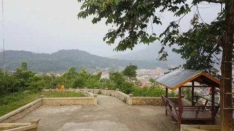 Monks walk down stair path, Lao town in valley surrounded by mountains, trees Stockbeeldmateriaal 76813180