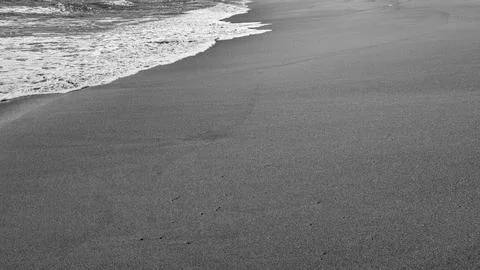 Monochrome high angle view captures glistening ocean water foam washing ont.. Stock Photos