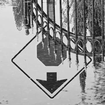 Monochrome reflection in street puddle stop sign, arrow, fence Stock Photos