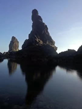 Monolithic rock formation casting a dark reflection on smooth water surface. Photos