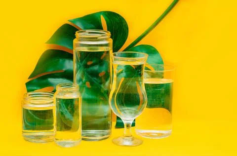 Monstera leaf distorted through glasses with water. Summer concept. Yellow ba Stock Photos