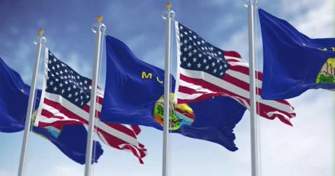 Montana state flags waving in the wind with the American flag on a clear day Stock Footage 273117455