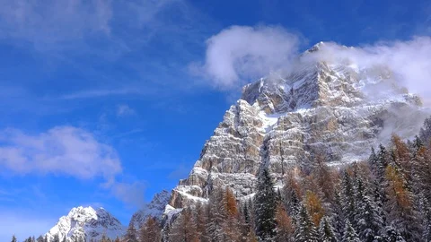 Monte Pelmo surrounded by trees, snow melting and clouds dissolving Stockbeeldmateriaal 129559947