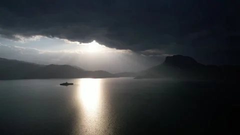 Moody aerial view of sunlight breaking through storm clouds over mountain Stock Footage 337885488