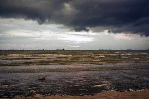 Moody Beach Sunset With Dark Clouds Over The Sea And Distant Ships Stock Photos