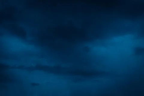 Moody, dramatic storm clouds fill a deep blue evening sky Stock Photos