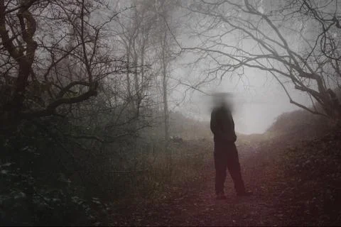 A moody figure with a blurred head standing in a forest on a foggy day Stock Photos