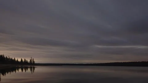 Moody gray clouds move through the night sky above a calm northern lake Stock Footage 253809376