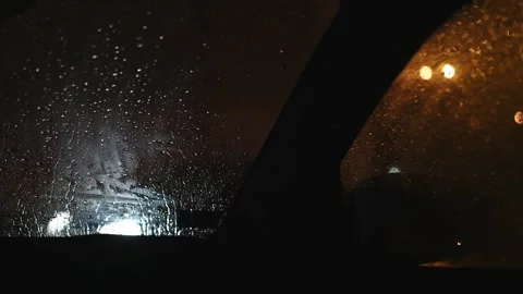 Moody nighttime view through a rain-soaked car window, headlights and stree.. Stock Footage 336797459