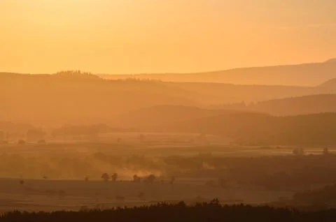 A moody sunset over a mountain range, fields shrouded in fog. Stock Photos