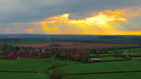 Moody sunset sky opening with bright golden light over patchwork farmland Stock-Footage 335369432