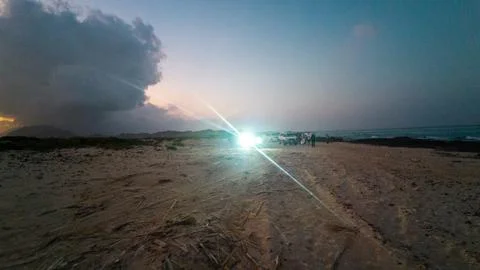 Moody twilight beach with storm clouds and car headlights Stock Photos