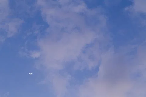 Moon behind the clouds during the day on a bright blue sky. Stock-Fotos